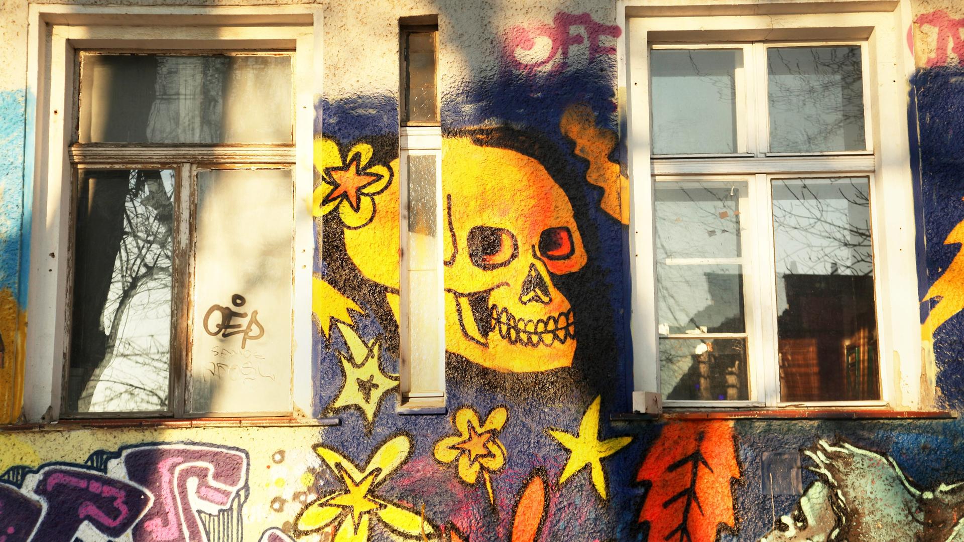 Ein gelber Totenkopf grinst als Wandbild zwischen zwei Fenstern.