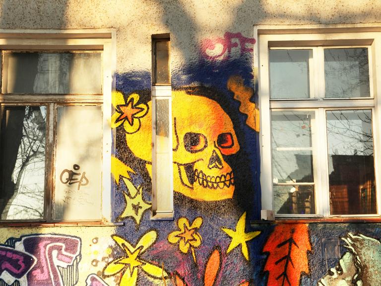 Ein gelber Totenkopf grinst als Wandbild zwischen zwei Fenstern.