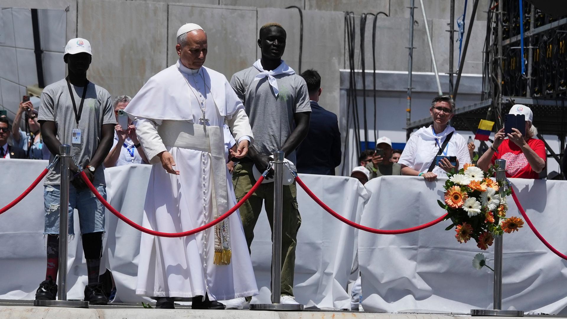Arguineguin: Papst Leo XIV. wirft einen Blumenstrauß ins Meer, flankiert von Migranten, während eines Treffens mit Organisationen, die mit Migranten arbeiten.