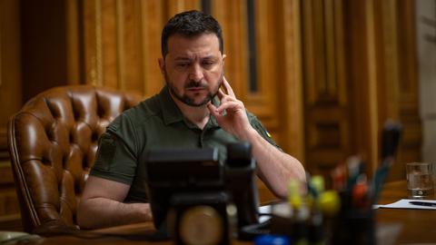 Der ukrainische Präsident Wolodymyr Selenskyj sitzt an einem Schreibtisch und schaut auf ein Telefon.