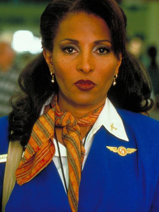 Filmstill aus "Jackie Brown" von Quentin Tarantino aus dem Jahr 1997. Die Schauspielerin Pam Grier in Stewardess Uniform mit entschlossenem ernsten Blick.