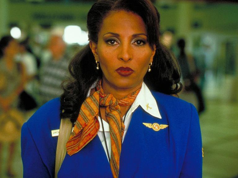 Filmstill aus "Jackie Brown" von Quentin Tarantino aus dem Jahr 1997. Die Schauspielerin Pam Grier in Stewardess Uniform mit entschlossenem ernsten Blick.
