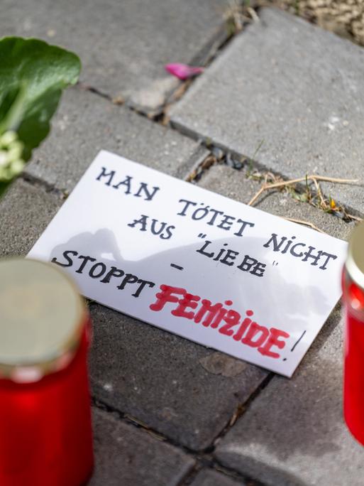 Blumen und Kerzen liegen nach einem tödlichen Messerangriff vor einem Hauseingang in Berlin-Friedrichsfelde neben einem Zettel mit der Aufschrift „Man tötet nicht aus Liebe - Stoppt Femizide“.
