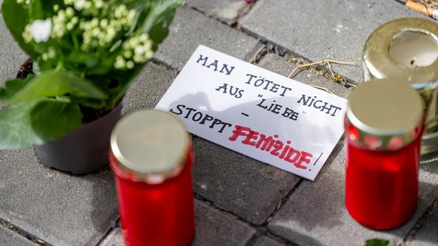 Blumen und Kerzen liegen nach einem tödlichen Messerangriff vor einem Hauseingang in Berlin-Friedrichsfelde neben einem Zettel mit der Aufschrift „Man tötet nicht aus Liebe - Stoppt Femizide“.