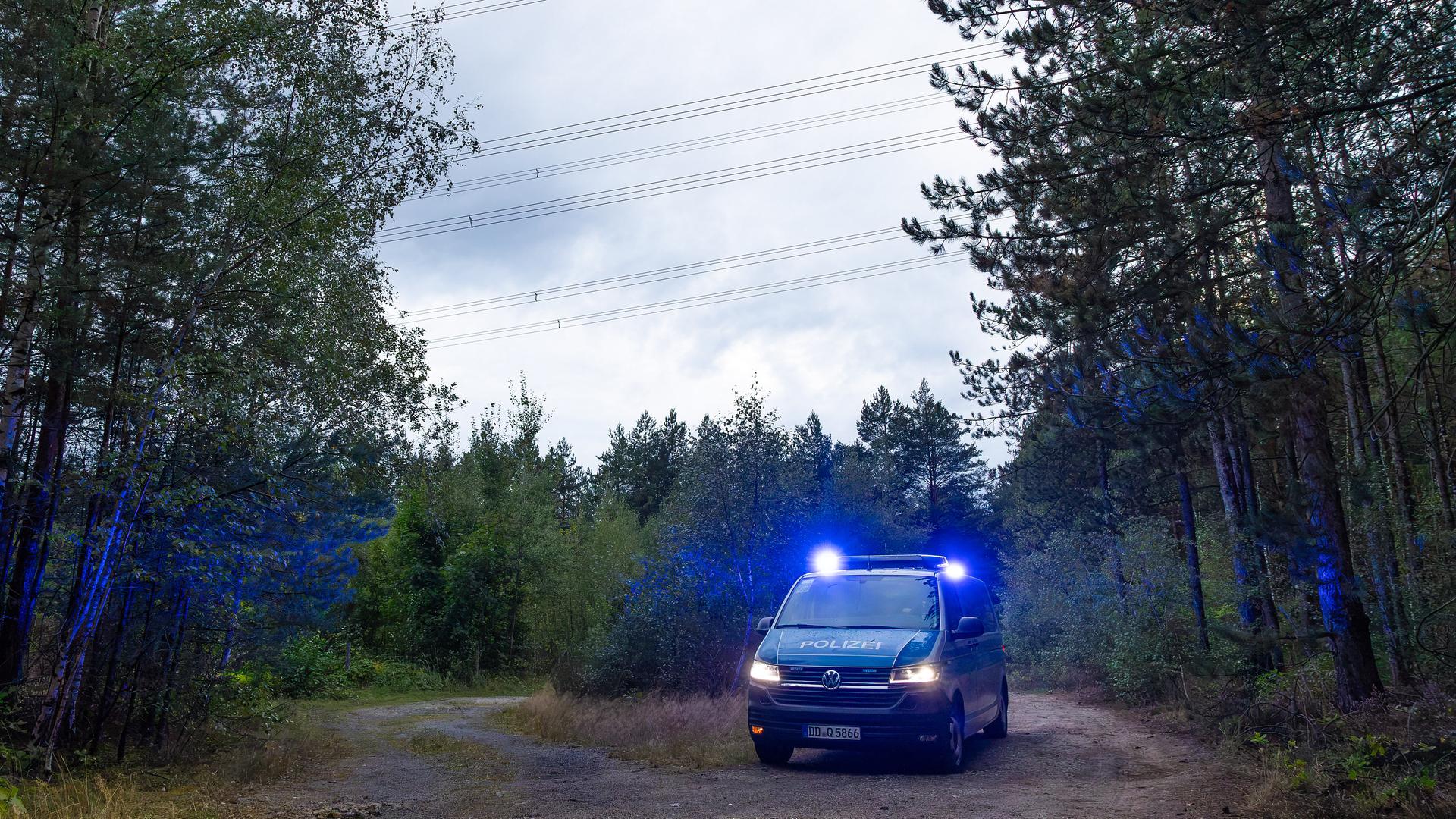 Ein VW-Bus der Polizei steht mit Blaulicht unter Hochspannungsleitungen vor einem Waldstück