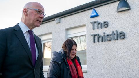 Der schottische Ministerpräsident John Swinney und die Vorsitzende des Stadtrats von Glasgow, Susan Aitken stehen vor einer Hauswand mit der Aufschrift "The Thistle".
