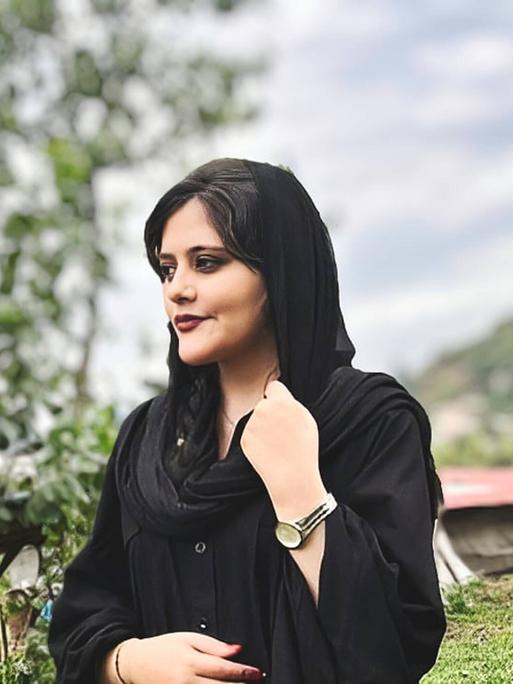 Jina Mahsa Amini  steht auf einem Hügel und blickt nach rechts. Sie trägt ein lockeres schwarzes Kopftuch.