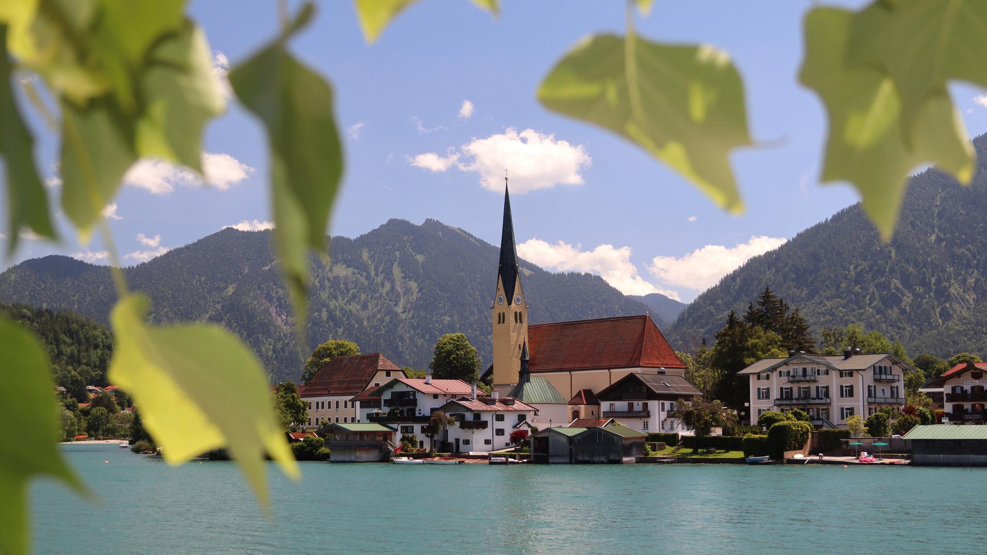 Blick auf den Tegernsee und die Kirche St.Laurentius in Rottach-Egern an einem Sommertag mit Blättern umrahmt.