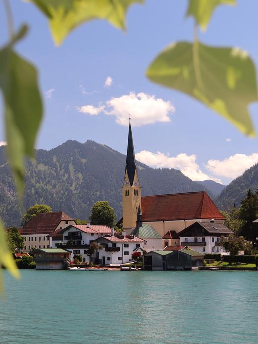 Blick auf den Tegernsee und die Kirche St.Laurentius in Rottach-Egern an einem Sommertag mit Blättern umrahmt.
