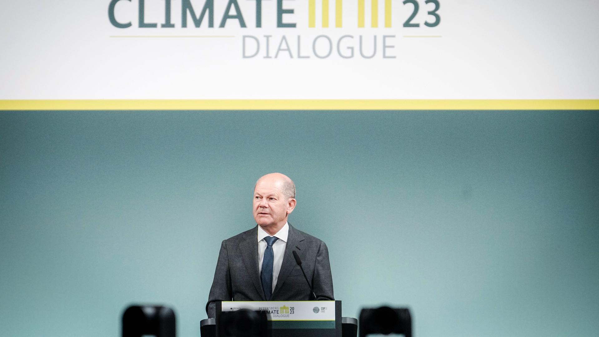 Scholz spricht an einem Rednerpult. Darüber ein Schild mit dem Logo des Klimadialogs.