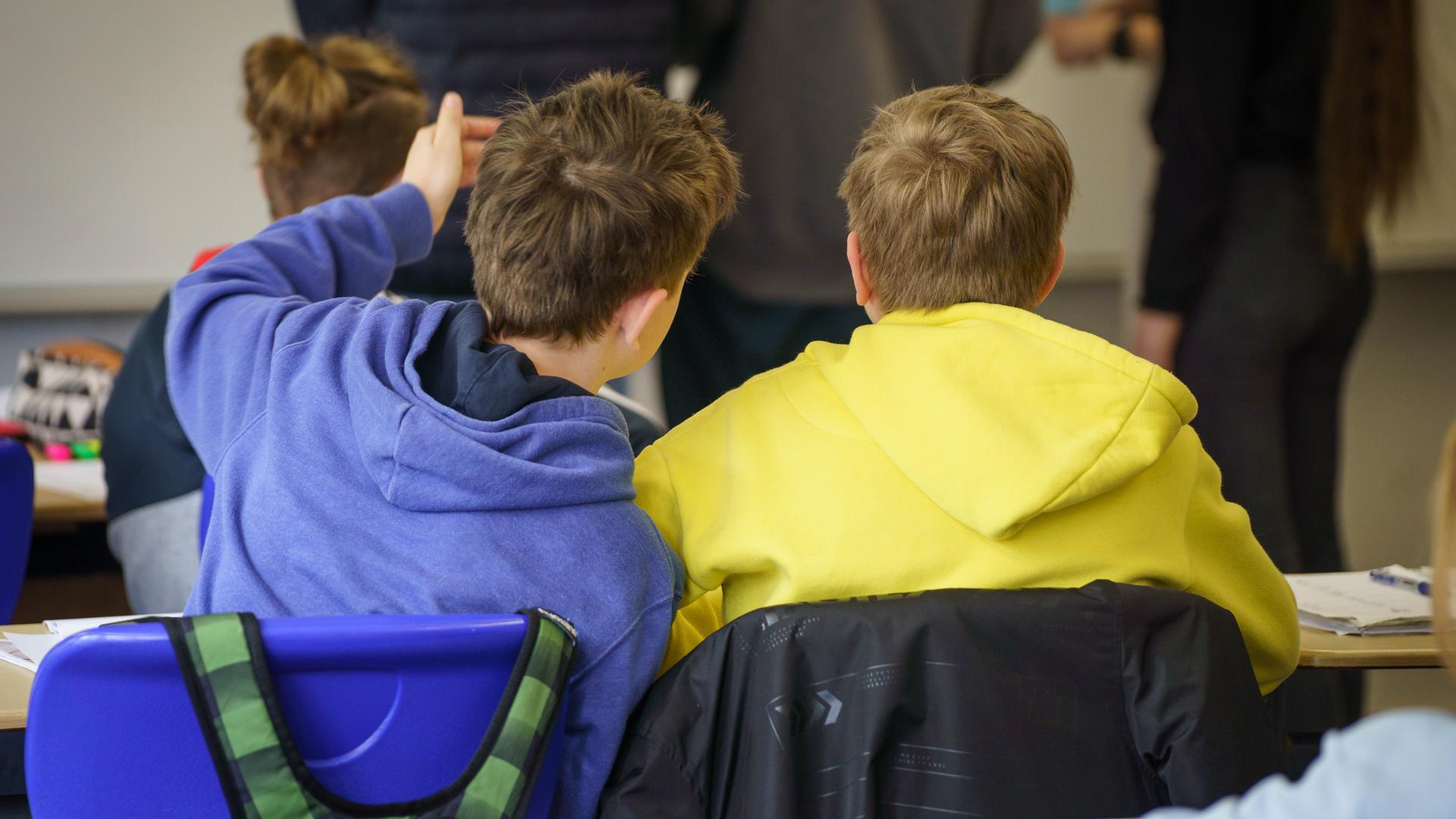 Zwei aus der Ukraine geflüchtete Schüler sitzen in einem Gymnasium an einem Tisch. Der eine trägt einen blauen Pulli, der andere einen gelben - die Nationalfarben der Ukraine.