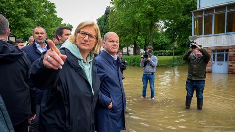 Bundeskanzler Scholz (re.) und die saarländische Ministerpräsidentin Rehlinger stehen in Gummistiefeln und umringt von Pressevertretern in der überschwemmten Gemeinde Kleinblittersdorf im Saarland.