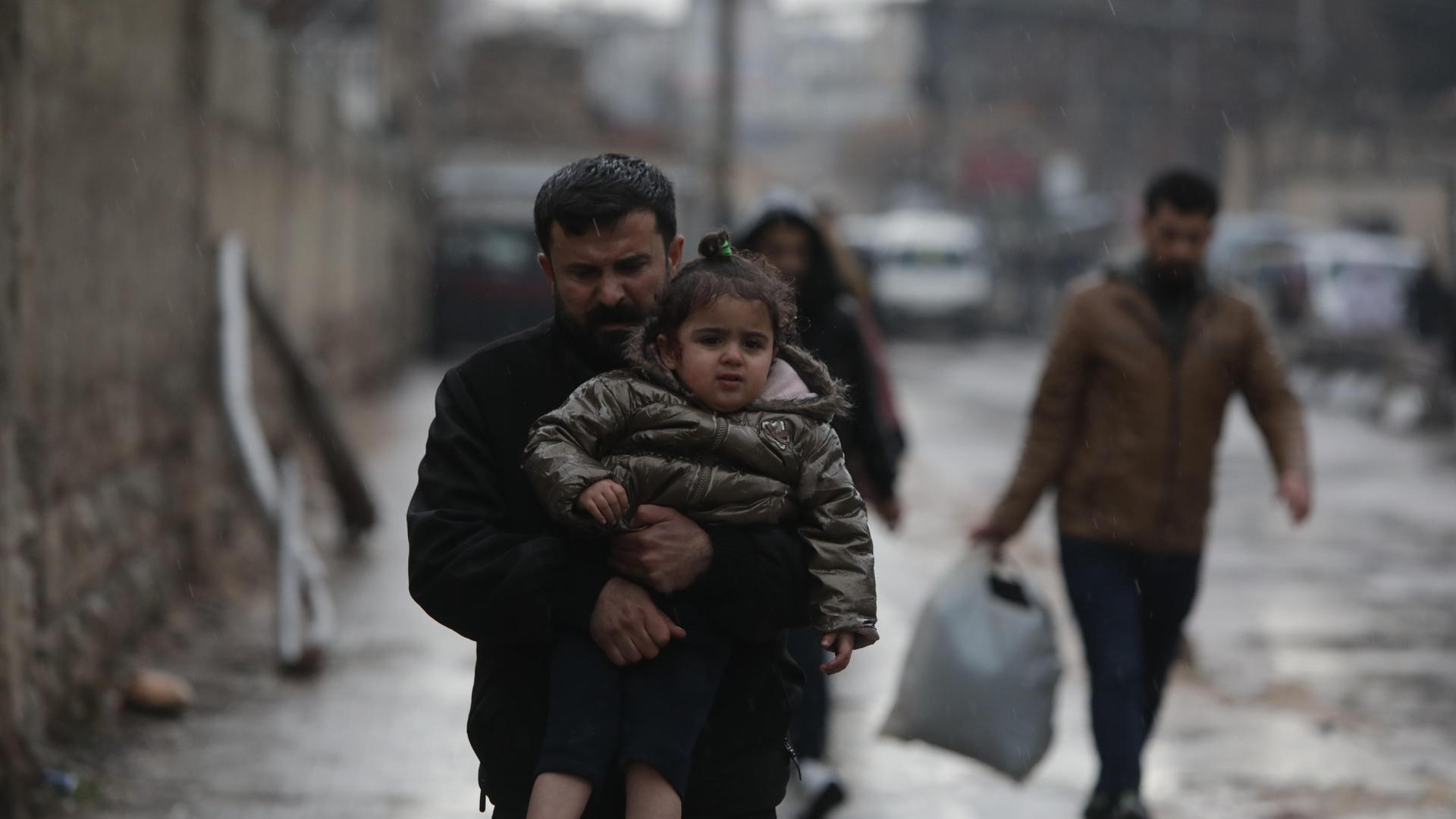 in Mann trägt sein Kind auf den Armen. Es regnet.