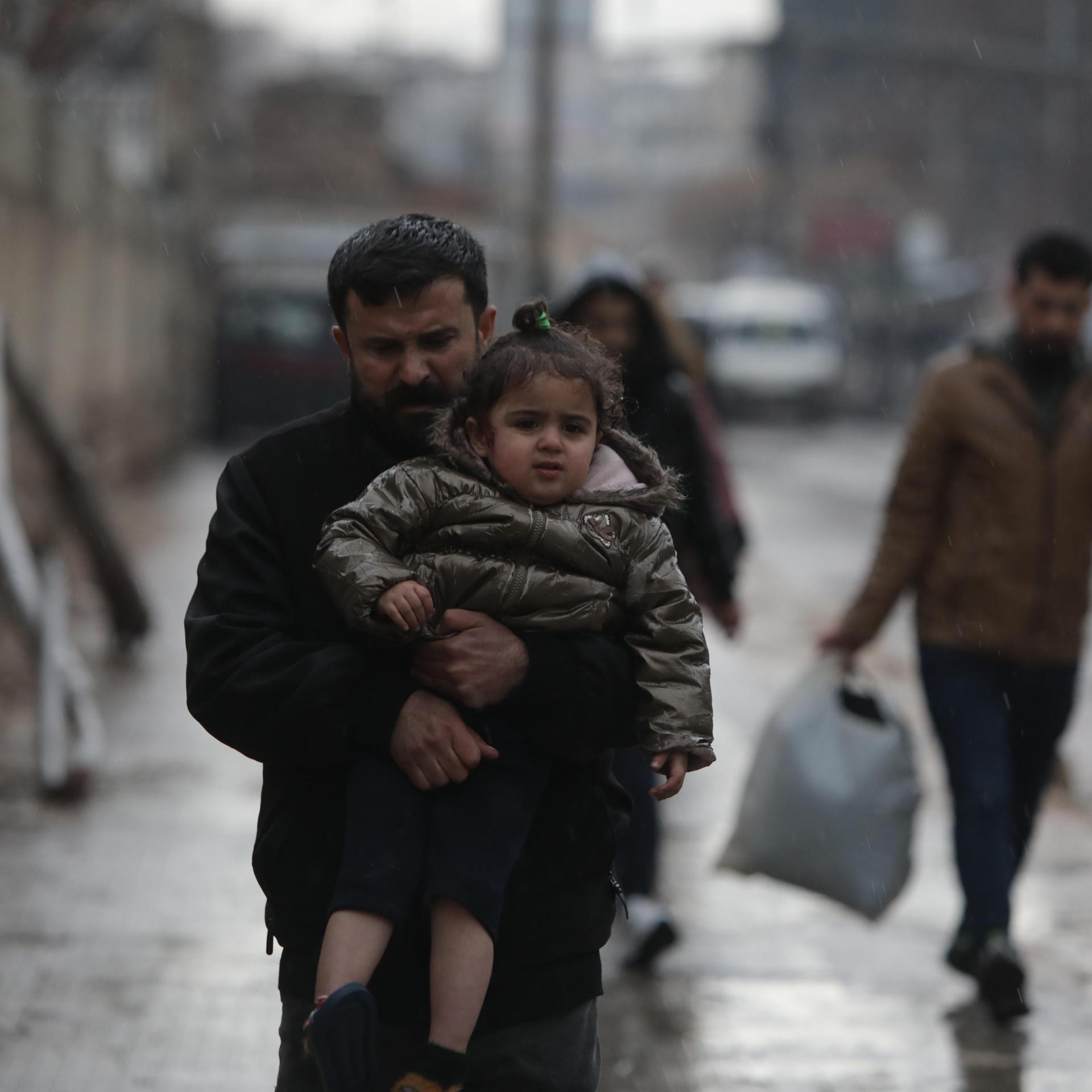 in Mann trägt sein Kind auf den Armen. Es regnet.