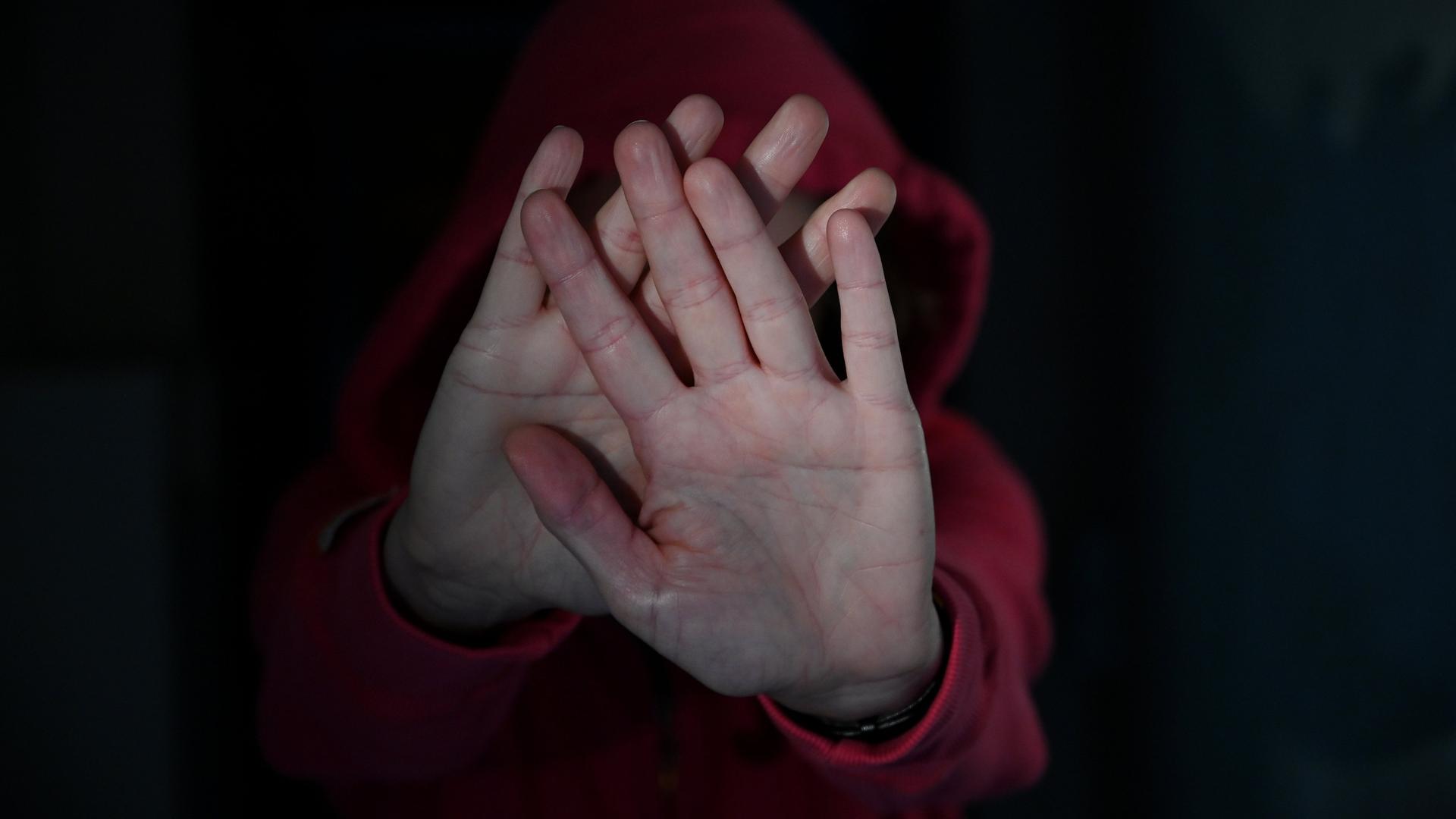 Eine Frau versucht, sich vor Gewalt zu schützen (gestellte Szene) und streckt zur Abwehr die Hände nach vorne