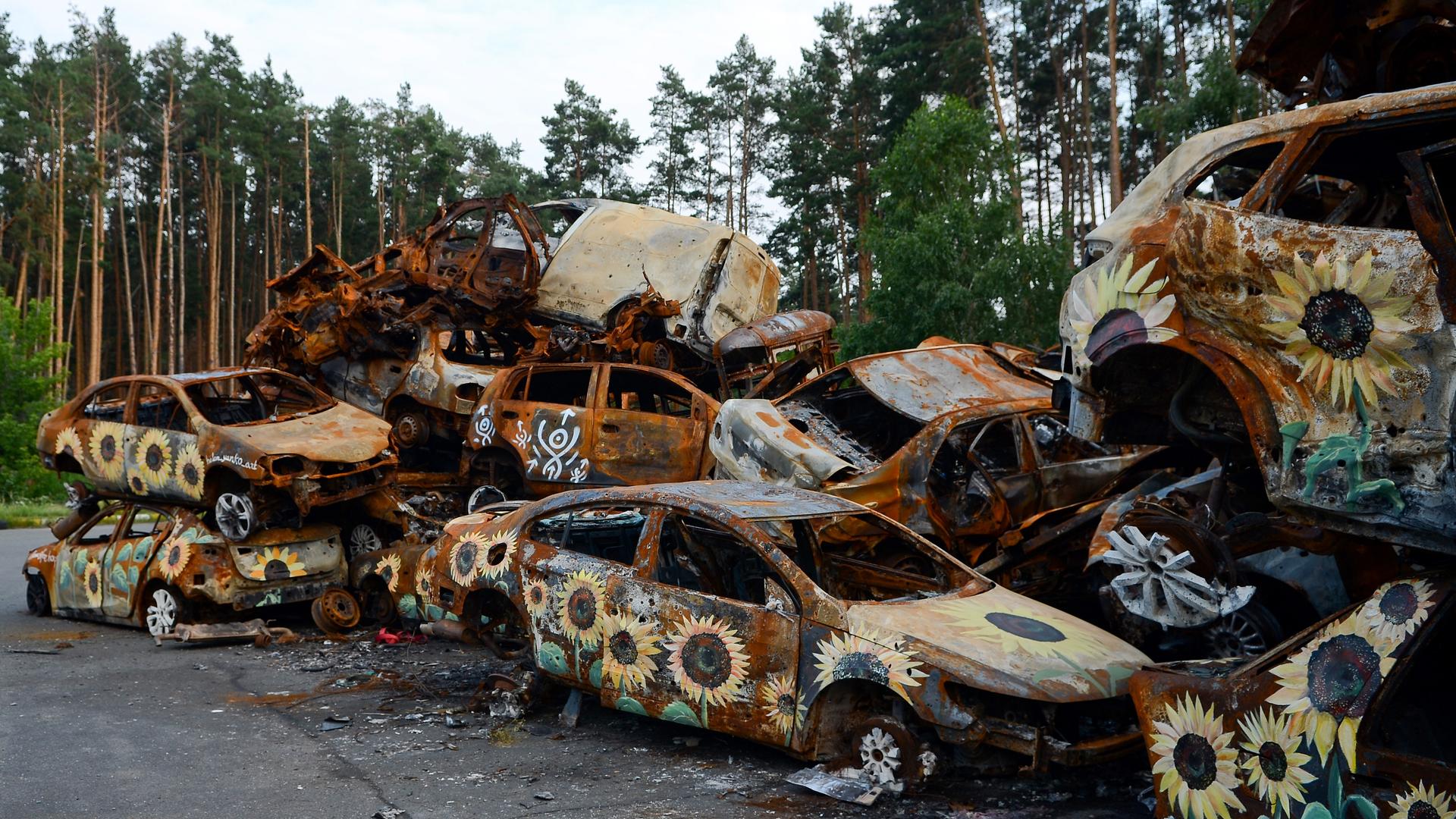 Auf durch den russischen Angriff auf die Ukraine ausgebrannten Autos sind Sonnenblumen gemalt.