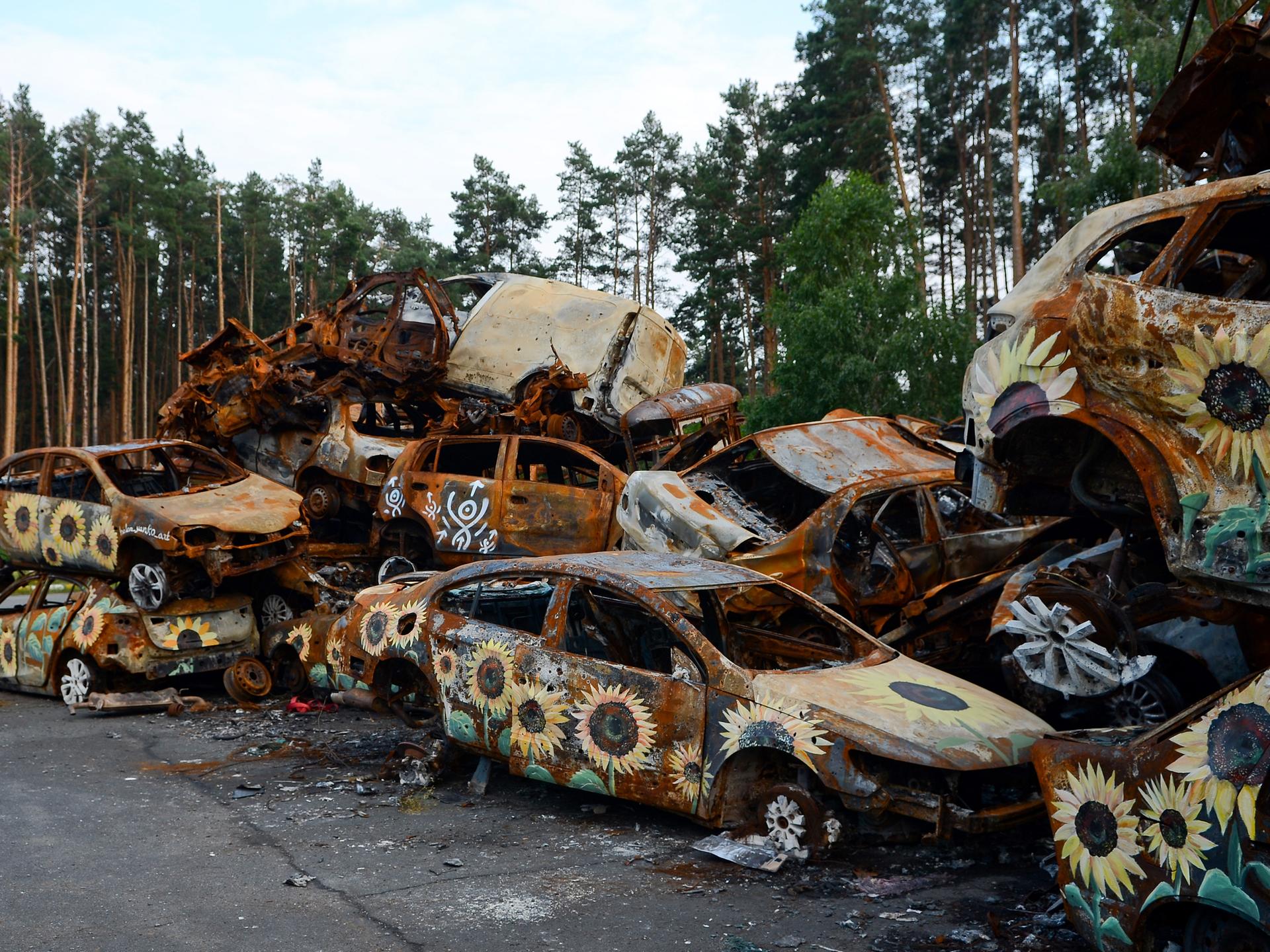 Auf durch den russischen Angriff auf die Ukraine ausgebrannten Autos sind Sonnenblumen gemalt.