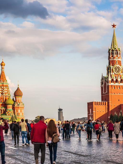 Menschen spazieren über den Roten Platz in Moskau: Die Basilius-Kathedrale (li.) und der Kreml (re.) in der Abenddämmerung. 