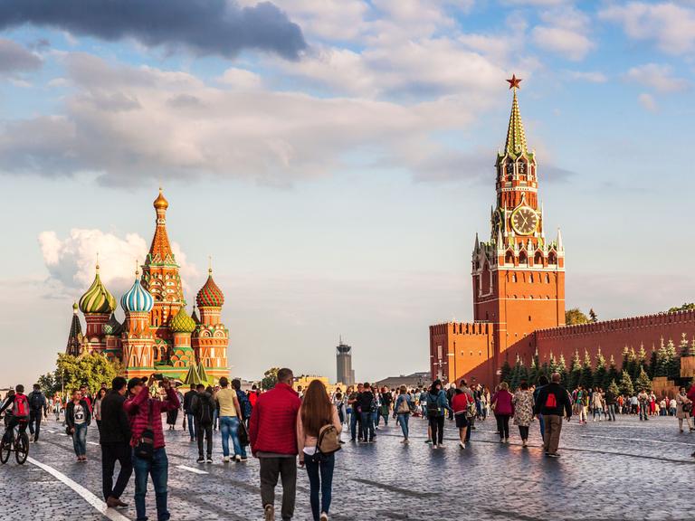 Menschen spazieren über den Roten Platz in Moskau: Die Basilius-Kathedrale (li.) und der Kreml (re.) in der Abenddämmerung. 