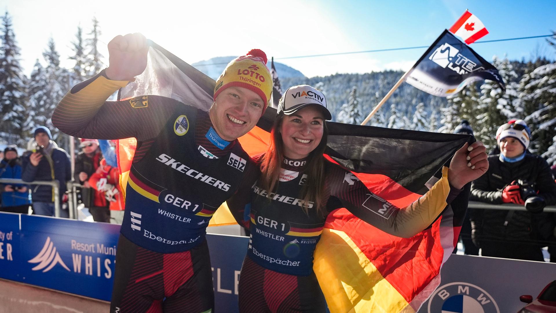 Die Rennrodler Max Langenhan und Julia Taubitz halten die deutsche Flagge in den Händen und lächeln. Die Rennrodler Max Langenhan und Julia Taubitz halten die deutsche Flagge in den Händen und lächeln.