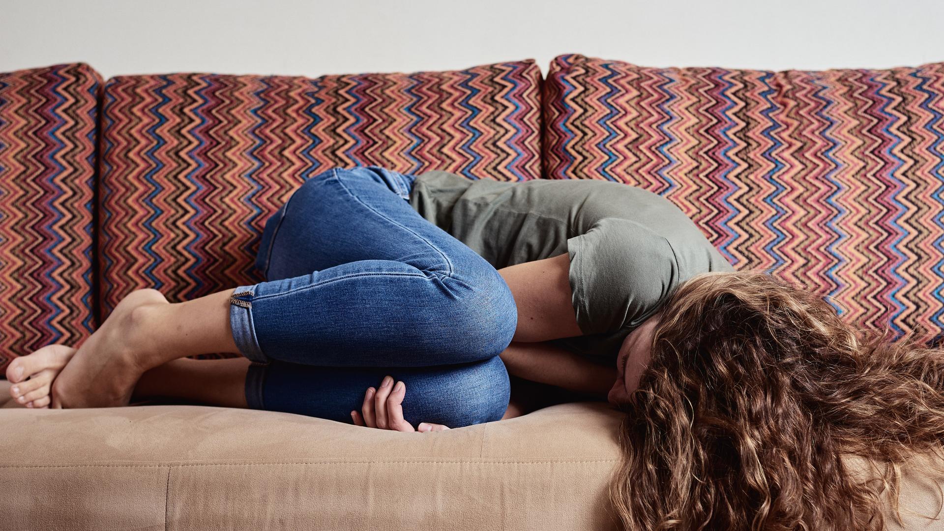 Eine Frau liegt vor Schmerzen zusammengekrümmt auf einem Sofa.