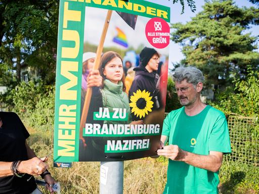 Mitglieder des Brandenburger Landtags hängen ein Wahlplakat auf, nachdem ein Wahlhelfer der Grünen in Hohen Neuendorf angegriffen und beraubt worden war, 14.08.2024.
