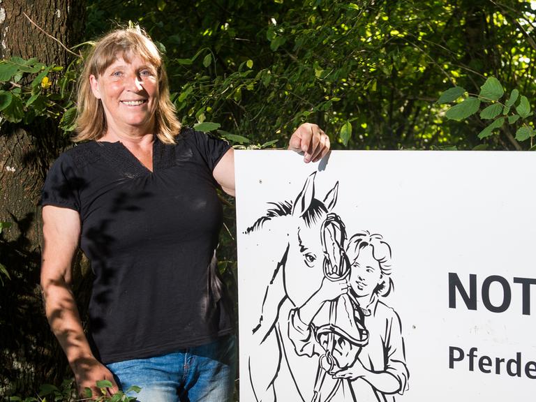 Pferdeklappe-Chefin Petra Teegen steht in Norderbrarup vor einem Schild mit der Aufschrift Notbox.