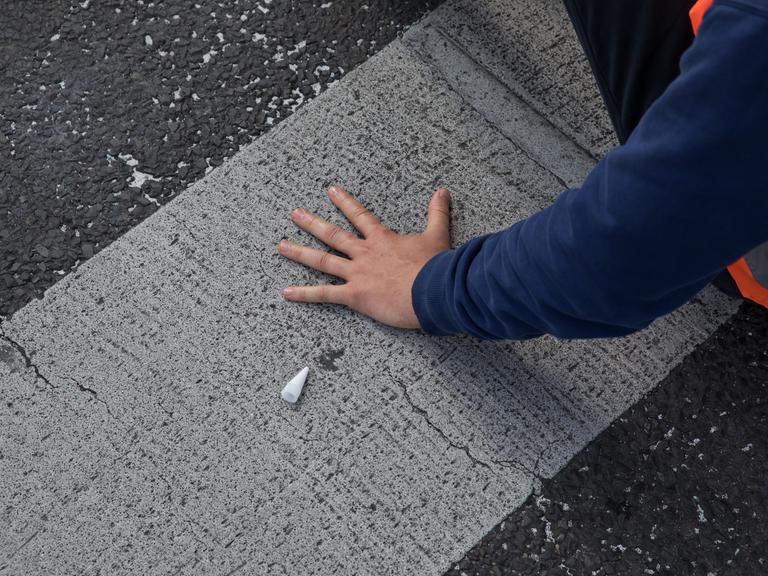 Ein Aktivist der Gruppe "Letzte Generation" hat seine linke Hand auf eine Straße geklebt, um diese zu blockieren.