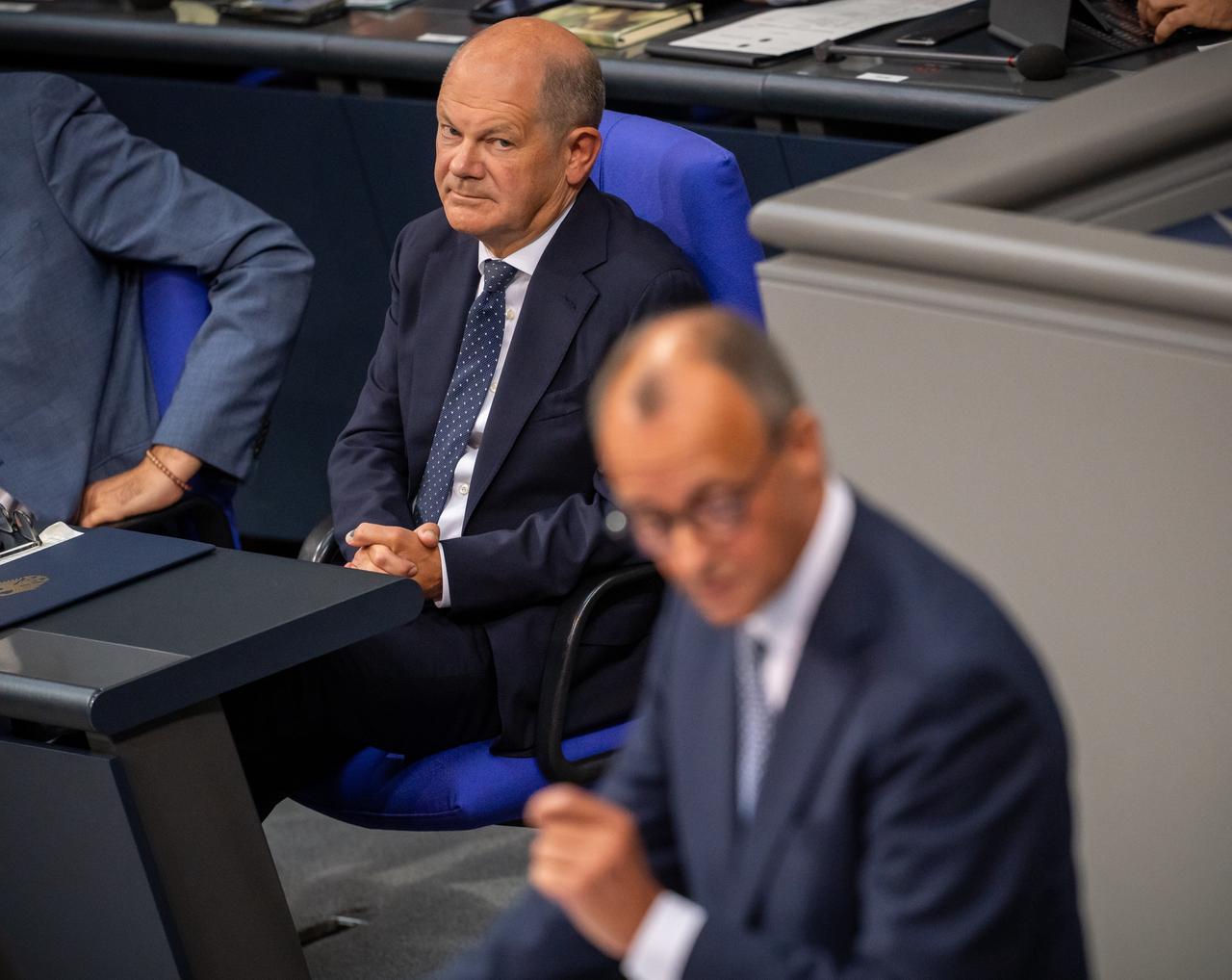 Olaf Scholz schaut zum auf dem Podium im Bundestag sprechenden Friedrich Merz.