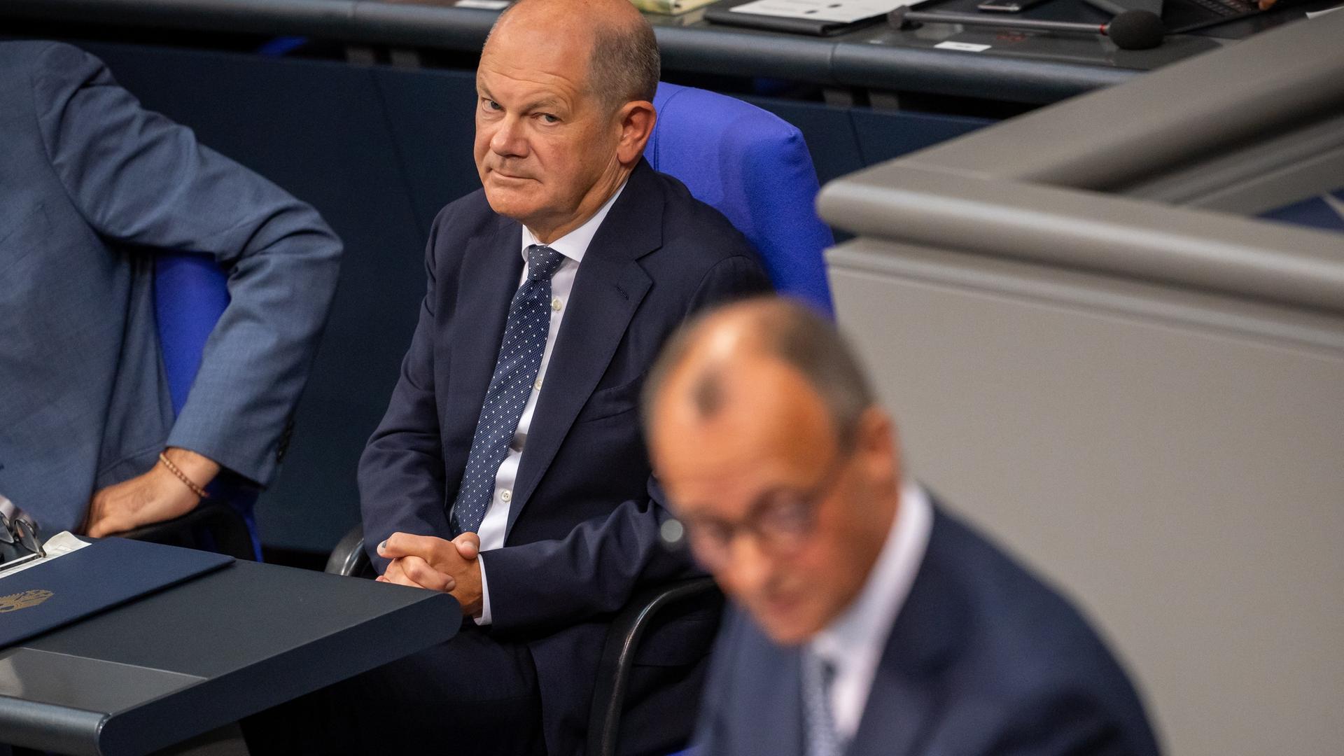 Olaf Scholz schaut zum auf dem Podium im Bundestag sprechenden Friedrich Merz.