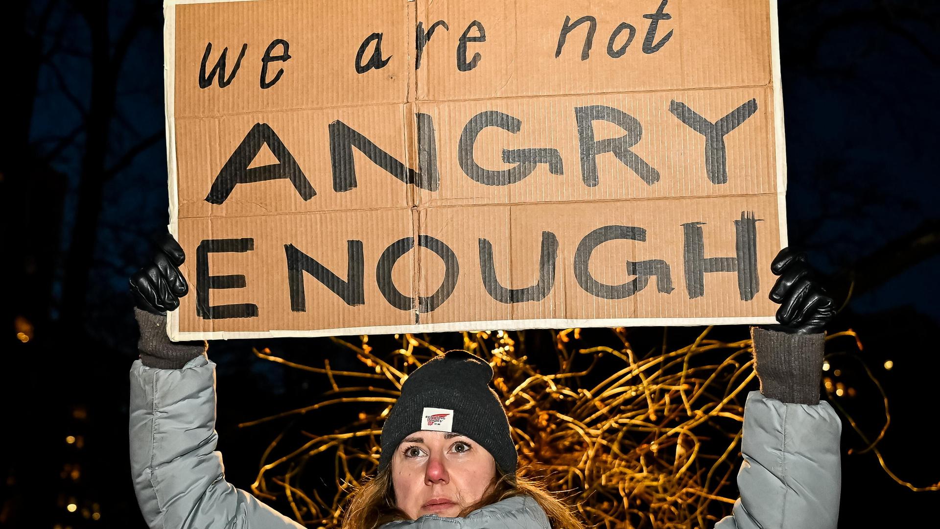 Eine Frau in Winterkleidung hält das Schild mit der Aufschrift "We are not angry enough" hoch