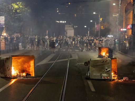Bei einem Protest in Belgrad liegen mehrere brennende Mülltonnen auf der Straße.