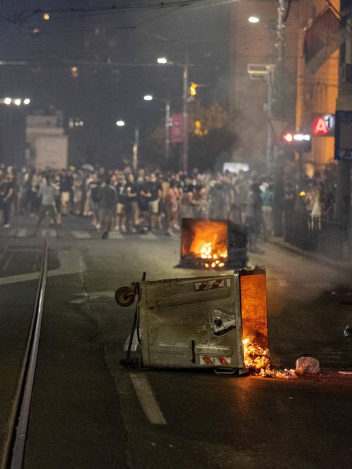 Bei einem Protest in Belgrad liegen mehrere brennende Mülltonnen auf der Straße.