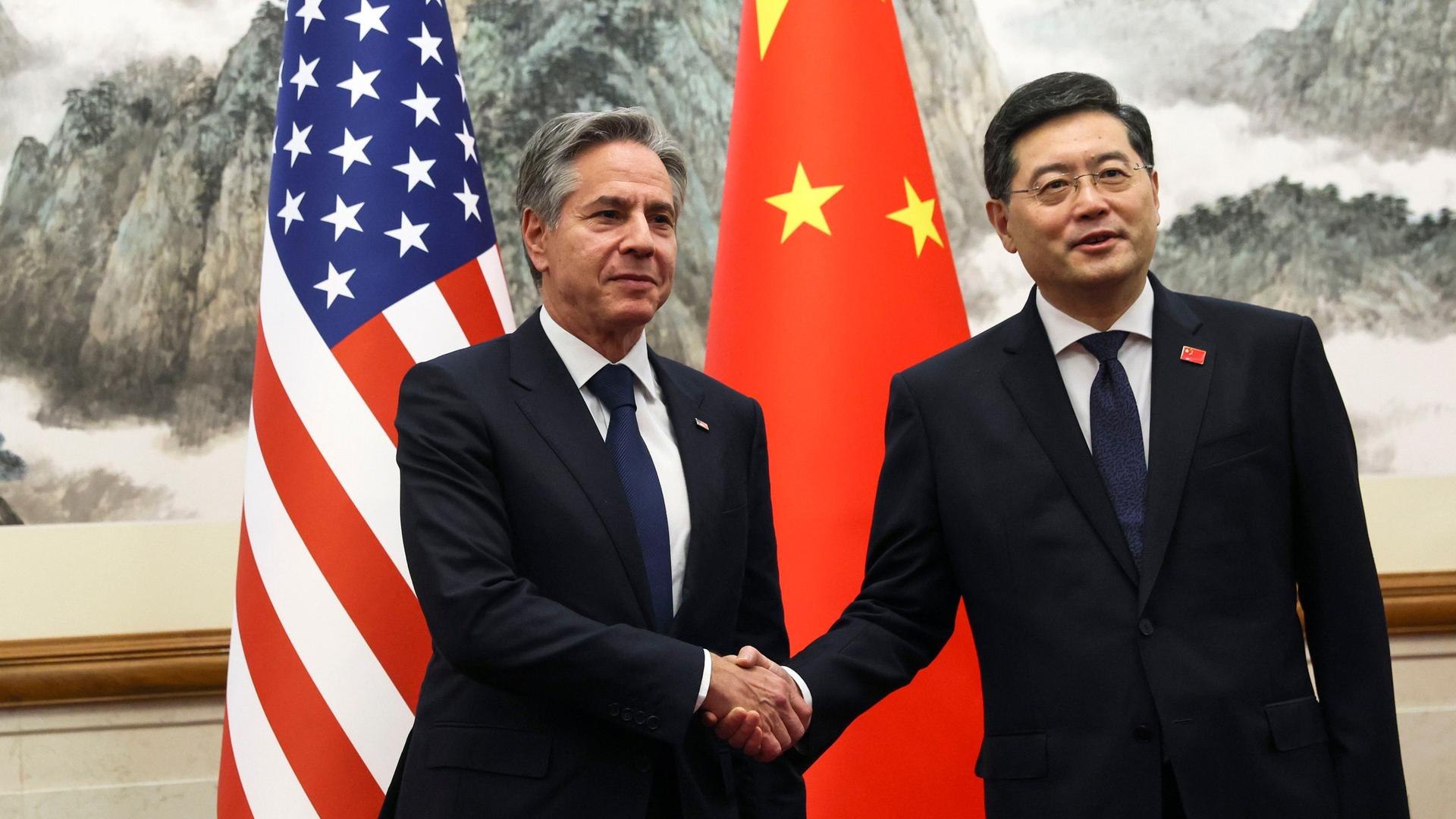 US-Außenminister Blinken schüttelt seinem chinesischen Amtskollegen Qin Gang die Hand. Im Hintergrund die Flaggen der beiden Länder. 