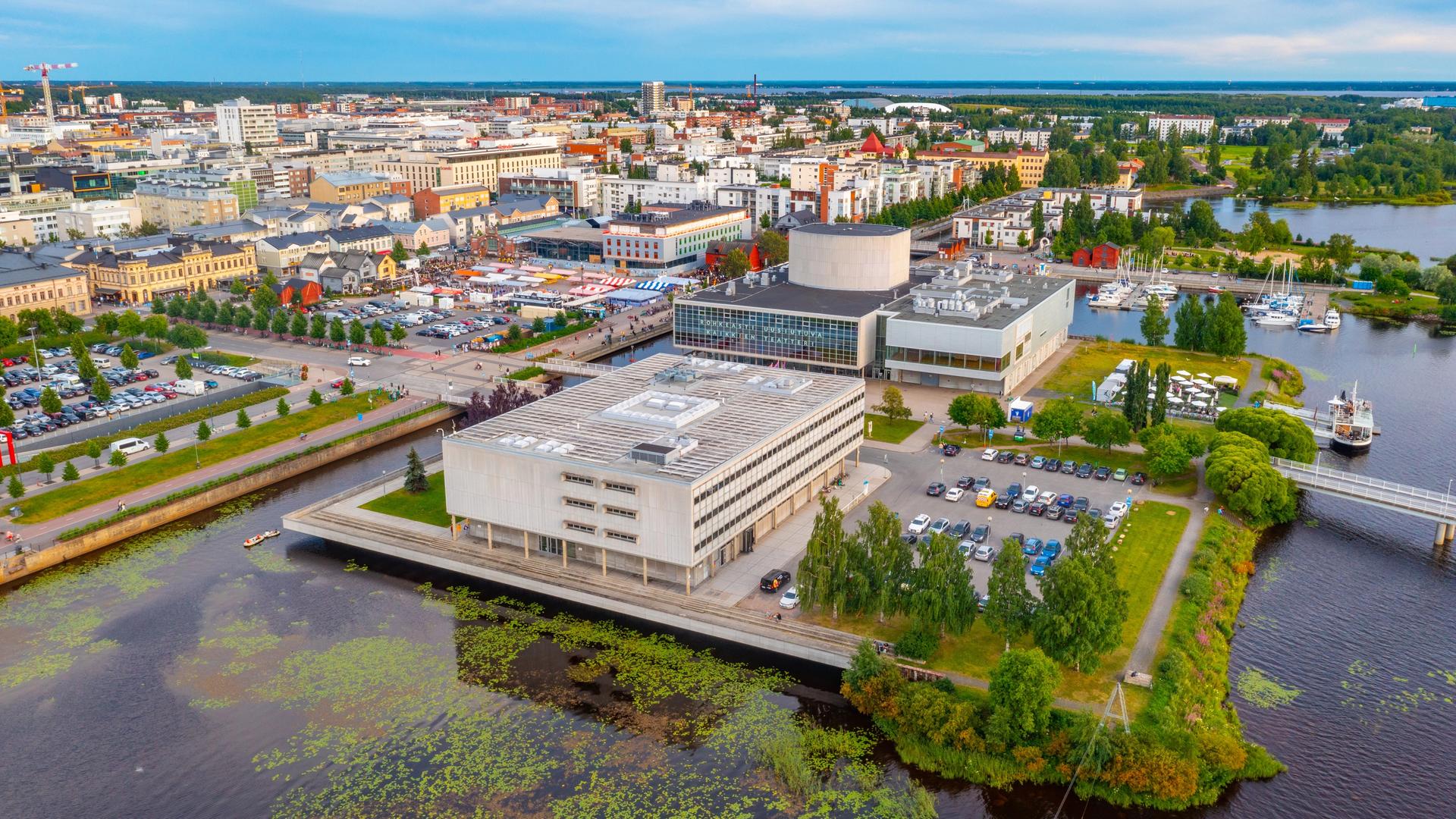 Panoramablick auf die finnische Stadt Oulu. Sie liegt am Wasser. Im Vordergrund sind große Gebäude aus Beton.