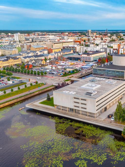 Panoramablick auf die finnische Stadt Oulu. Sie liegt am Wasser. Im Vordergrund sind große Gebäude aus Beton.