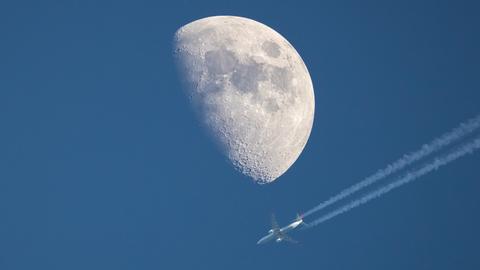 Ein Flugzeug fliegt nahe des dahinter liegenden Mondes vorbei.