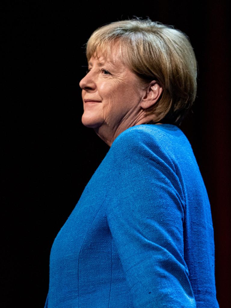 Seitliche Aufnahme der ehemaligen Bundeskanzlerin Angela Merkel (CDU) in einem blauen Blazer vor schwarzem Hintergrund.