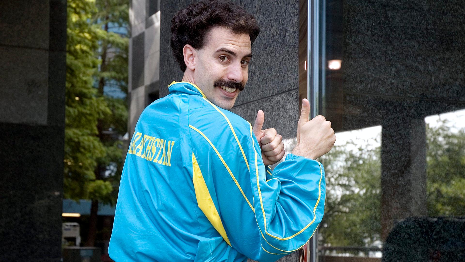 Der Schauspieler Sacha Baron Cohen als "Borat" in dem gleichnamigen Mockumentary-Film von 2006 schräg seitlich und teilweise von hinten zu sehen in einem blau-gelben Trainingsanzug auf dessen Rücken "Kasachstan" steht. Der Schauspieler Sacha Baron Cohen als "Borat" in dem gleichnamigen Mockumentary-Film von 2006 schräg seitlich und teilweise von hinten zu sehen in einem blau-gelben Trainingsanzug auf dessen Rücken "Kasachstan" steht.