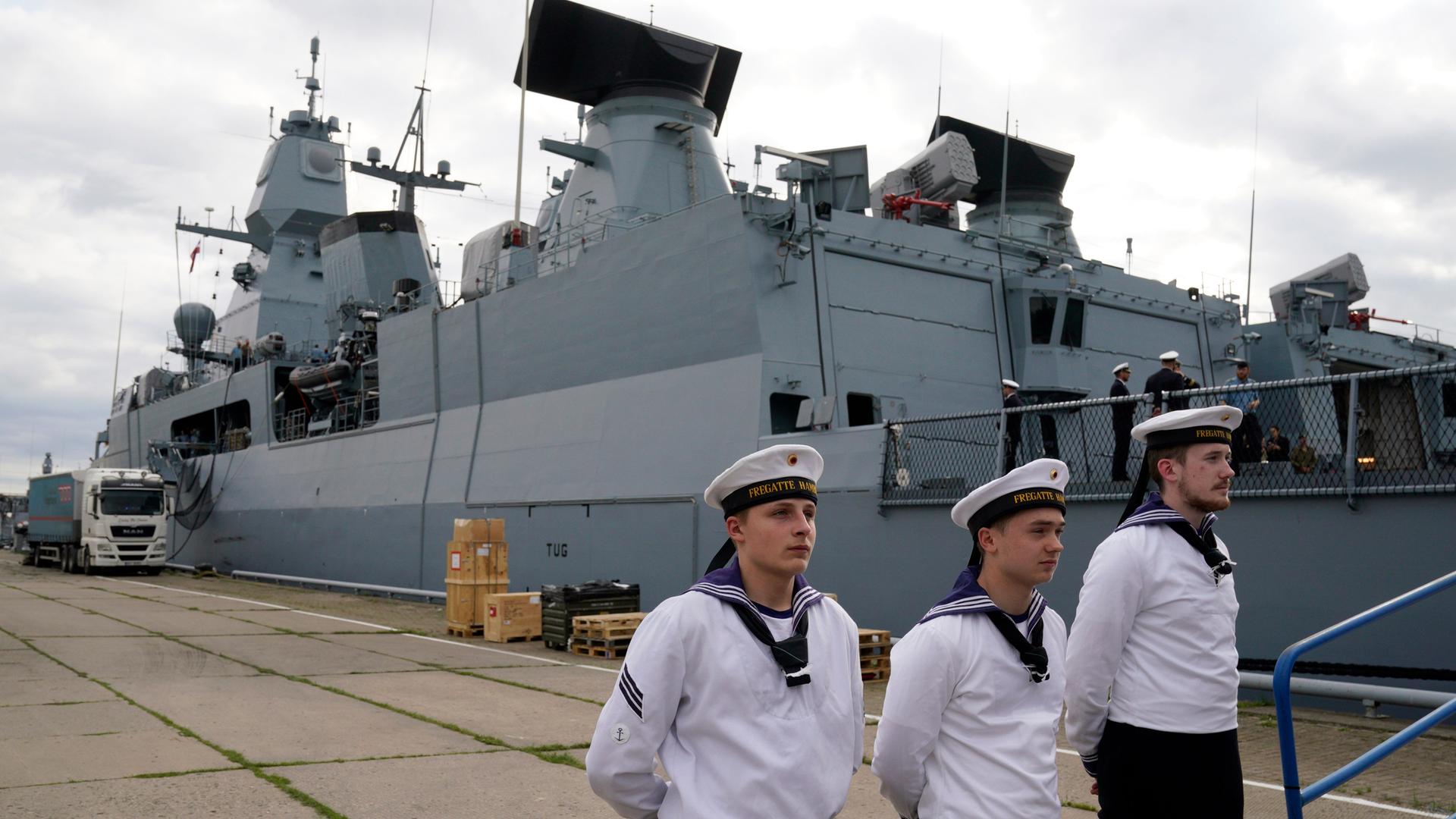 Drei Besatzungsmitglieder der deutschen Fregatte Hamburg stehen vor dem Schiff auf dem Kai.