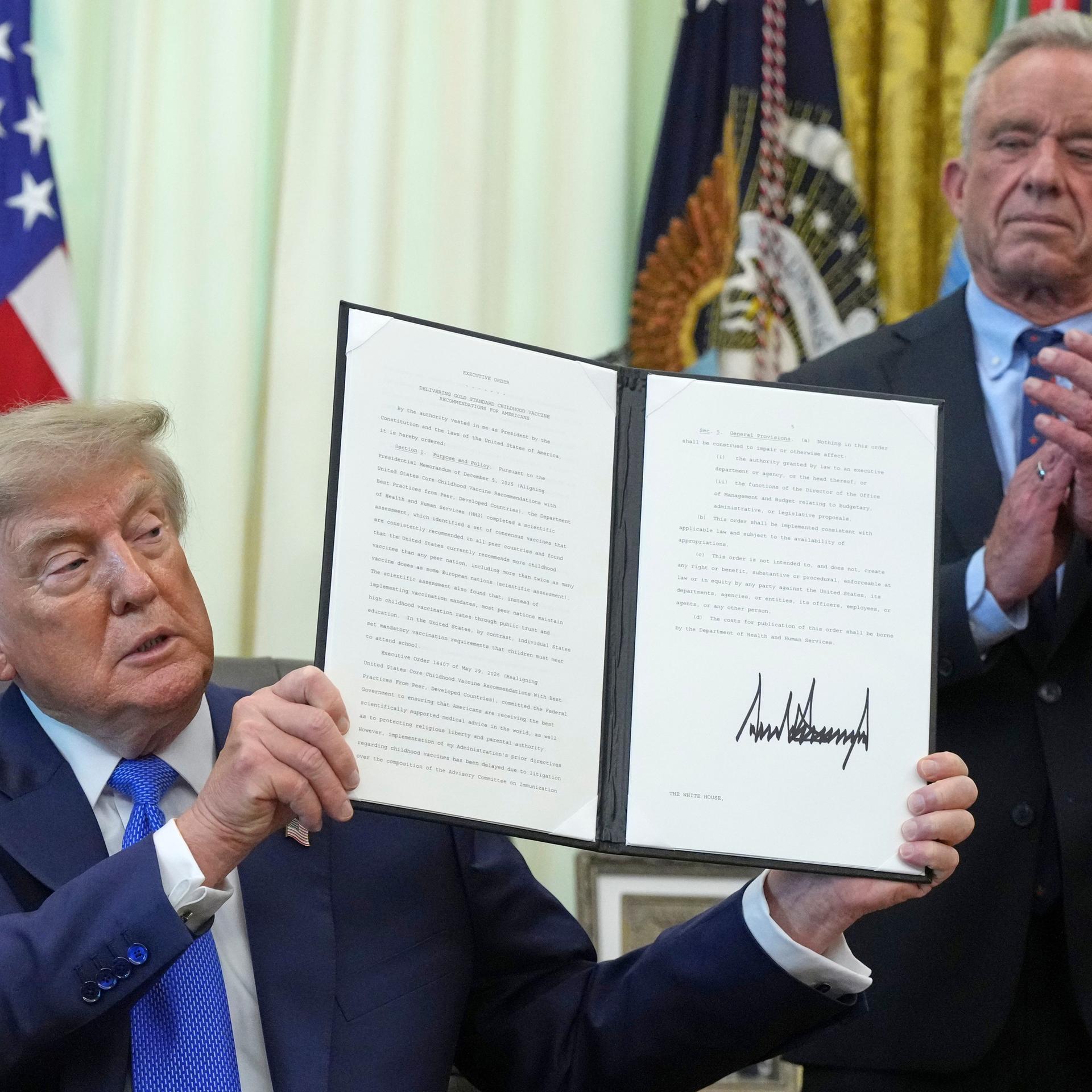 USA, Washington: US-Präsident Donald Trump hält eine unterzeichnete Exekutivanordnung zu Impfstoffen in der Hand, während Gesundheitsminister Robert F. Kennedy Jr. im Oval Office des Weißen Hauses applaudiert.