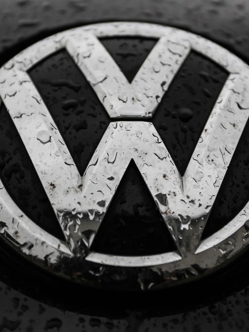 Das VW-Logo auf einem Auto ist von Regentropfen überzogen.