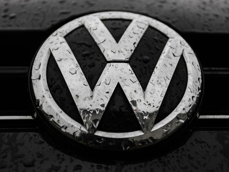 Das VW-Logo auf einem Auto ist von Regentropfen überzogen.