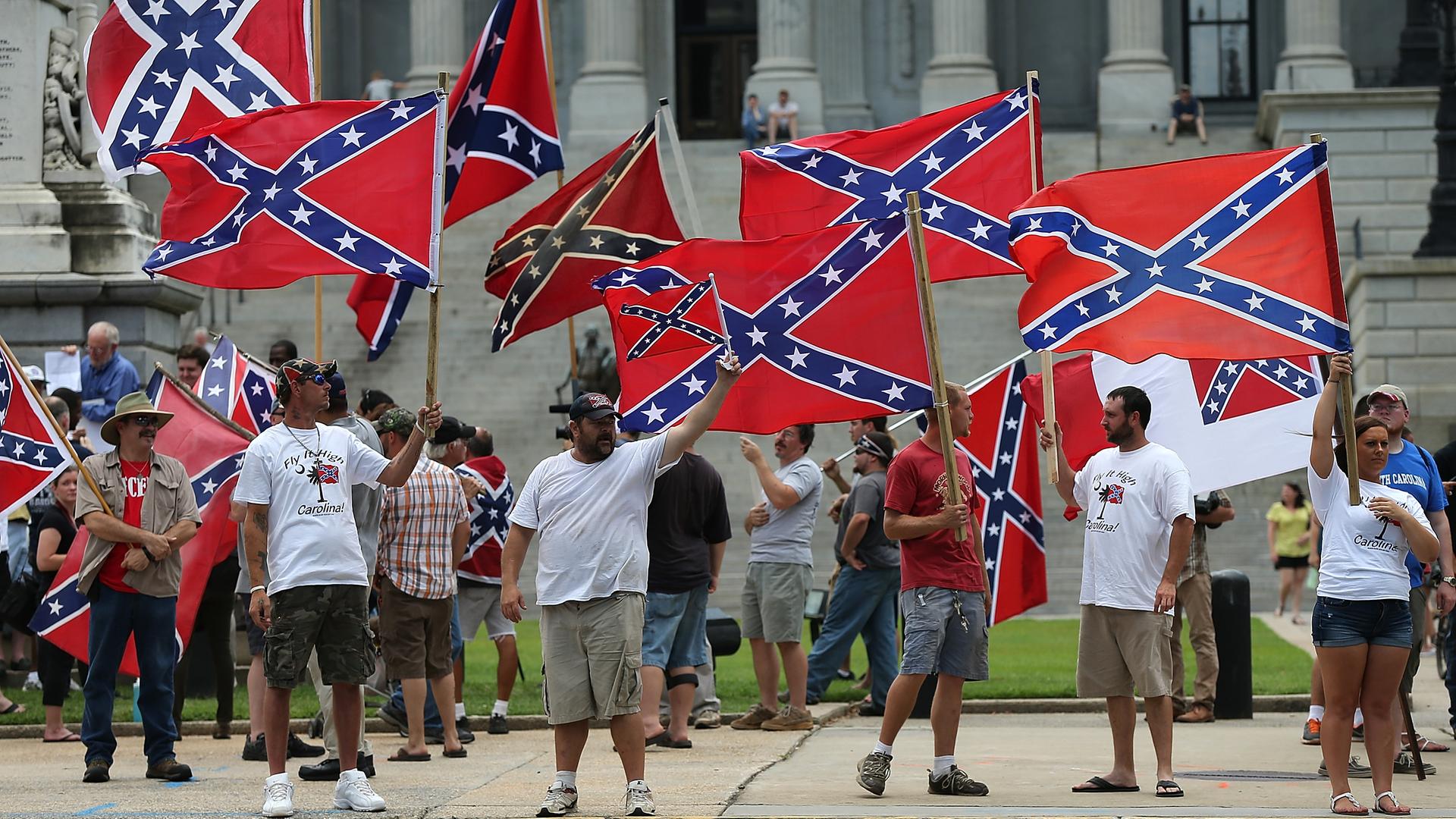 Demonstranten mit der Flagge der Konföderation (südstaaten Flagge) vor dem State House in South Carolina. Die Menschen stehen auf dem Bürgersteig und schwenken die Flaggen. (Symbolbild) Demonstranten mit der Flagge der Konföderation (südstaaten Flagge) vor dem State House in South Carolina. Die Menschen stehen auf dem Bürgersteig und schwenken die Flaggen. (Symbolbild)