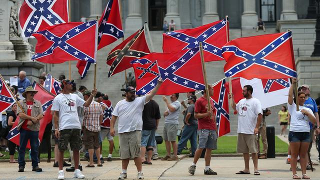 Demonstranten mit der Flagge der Konföderation (südstaaten Flagge) vor dem State House in South Carolina. Die Menschen stehen auf dem Bürgersteig und schwenken die Flaggen. (Symbolbild)