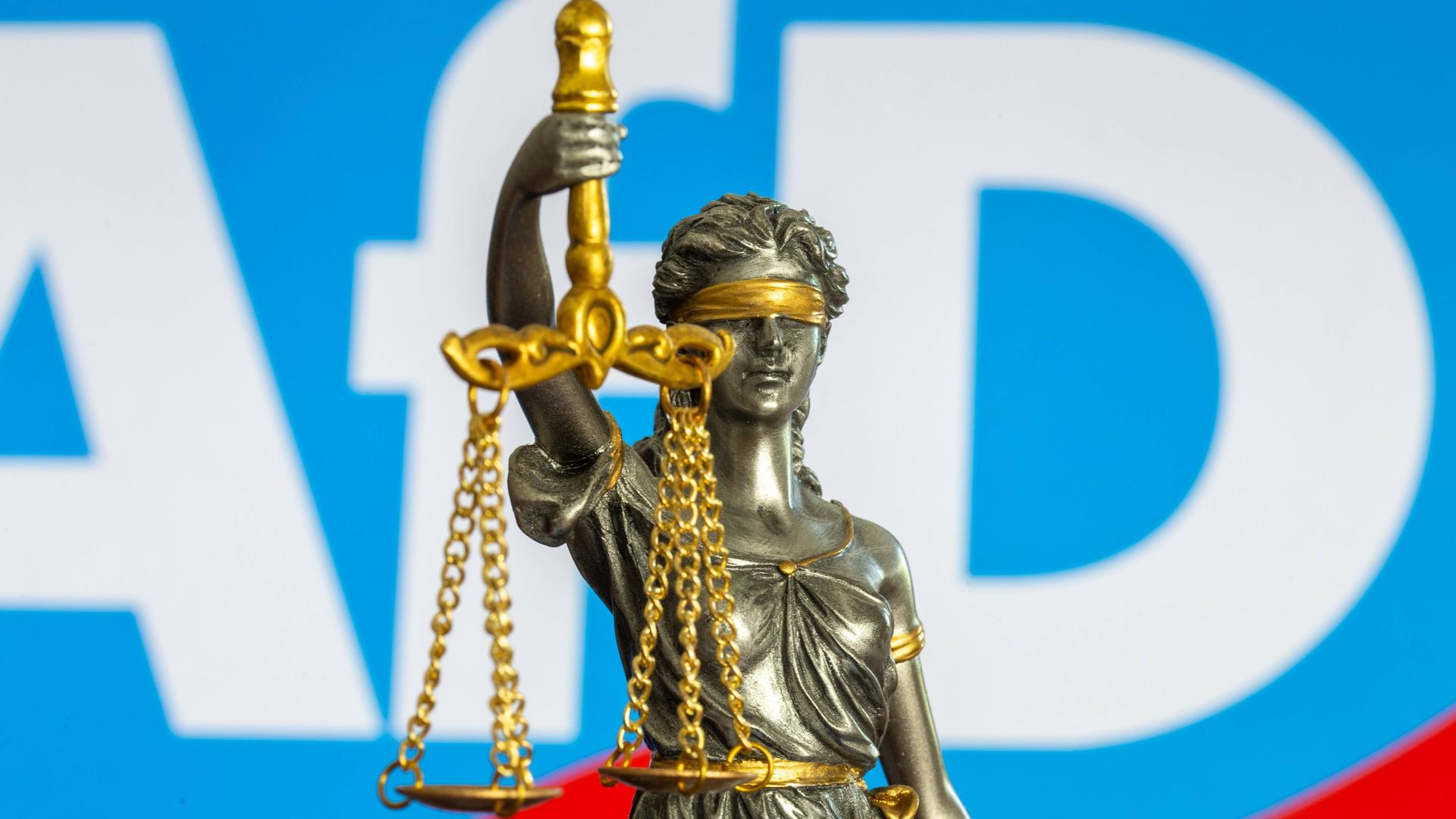 Die Bronzestatue der Justitia vor dem Logo der AfD – Symbolbild für den Rechtsstreit um die Einstufung der Partei als "gesichert rechtsextremistisch".
