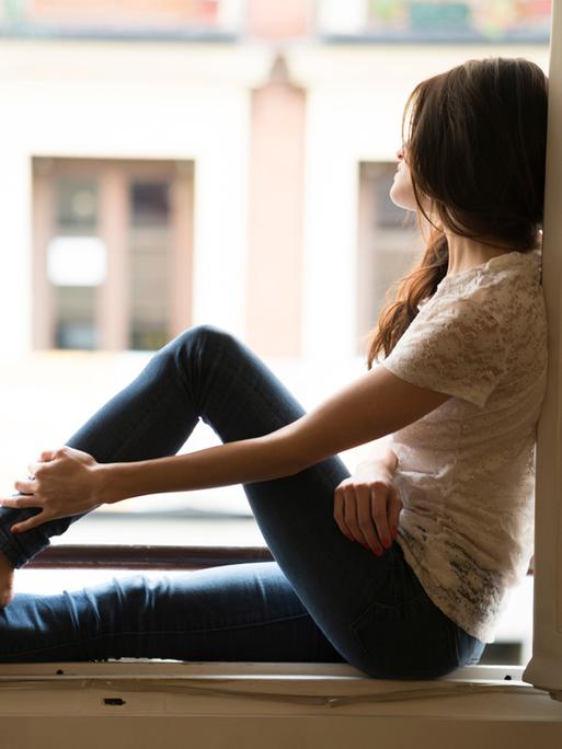 Eine Frau sitzt auf einer Fensterbank und schaut durchs offene Fenster