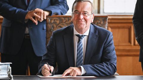 Boris Pistorius (SPD), Bundesverteidigungsminister, unterzeichnet in Bremen die Absichtserklärung zum Deployment Hub. Er sitzt an einem Tisch und lächelt in die Kamera. 