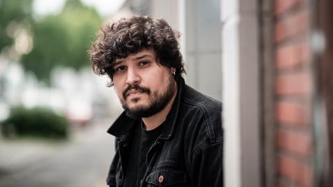 Canberk Köktürk blickt ernst in in die Kamera. Er hat dunkle Locken und trägt eine schwarze Jacke.