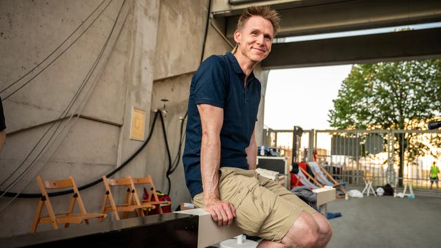 Der ehemalige Zehn-Kämpfer Frank Busemann sitzt an einem Rand von einem Stadion und lächelt.